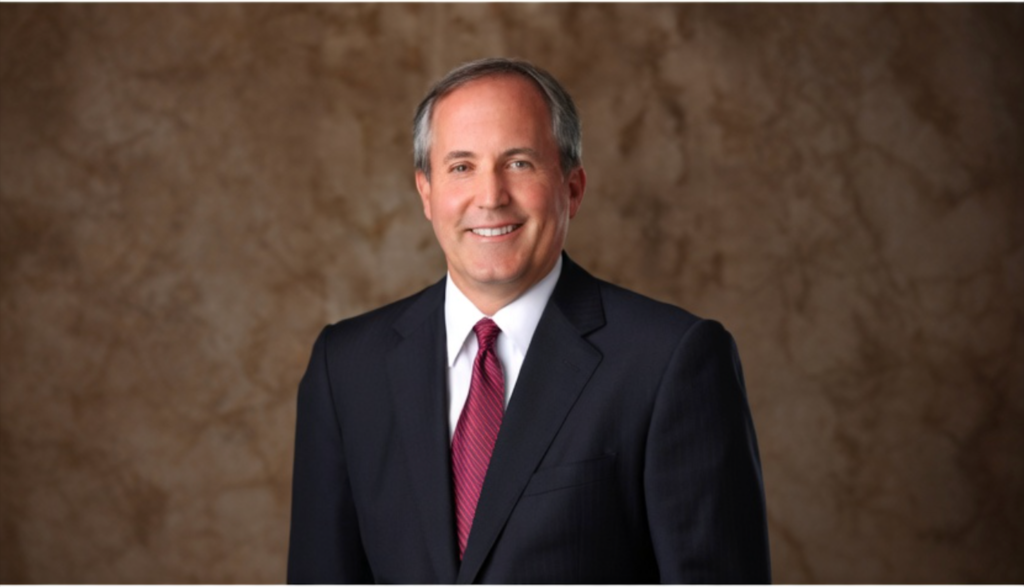 一名身着深色西装、白衬衫和红色条纹领带的男子站在棕色纹理背景前微笑。.